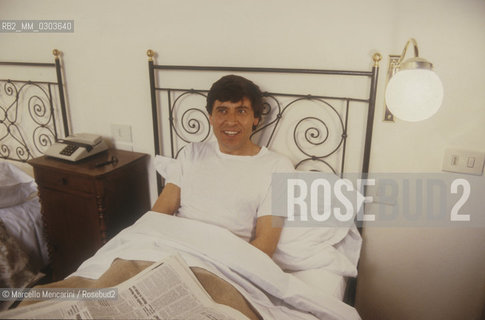Italian National Singers Football Team, 1987. Italian pop singer Gianni Morandi in bed in a hotel room during a tour of the talian National Singers Football Team / Nazionale italiana cantanti, 1987. Il cantante Gianni Morandi a letto in una camera dalbergo durante una tournée della Nazionale italiana cantanti - ©Marcello Mencarini/Rosebud2