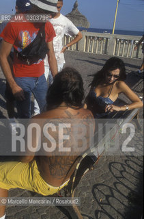 Ostia Lido, 1999. Tattooed man with iguana and other people. Ostia is a beach town near Rome. In the summer time many people from Rome go there to the sea, particularly young suburban people said in slang coatti / Lido di Ostia, 1999. Uomo tatuato con uniguana e altre persone. Ostia è la spiaggia dei romani. Destate è frequentata in particolare dai giovani che abitano le borgate della periferia, i cosiddetti coatti- ©Marcello Mencarini/Rosebud2
