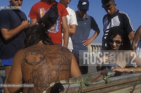 Ostia Lido, 1999. Tattooed man with iguana and other people. Ostia is a beach town near Rome. In the summer time many people from Rome go there to the sea, particularly young suburban people said in slang coatti / Lido di Ostia, 1999. Uomo tatuato con uniguana e altre persone. Ostia è la spiaggia dei romani. Destate è frequentata in particolare dai giovani che abitano le borgate della periferia, i cosiddetti coatti- ©Marcello Mencarini/Rosebud2