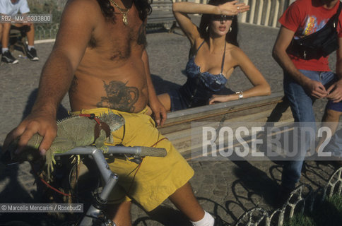Ostia Lido, 1999. Tattooed man with iguana and other people. Ostia is a beach town near Rome. In the summer time many people from Rome go there to the sea, particularly young suburban people said in slang coatti / Lido di Ostia, 1999. Uomo tatuato con uniguana e altre persone. Ostia è la spiaggia dei romani. Destate è frequentata in particolare dai giovani che abitano le borgate della periferia, i cosiddetti coatti- ©Marcello Mencarini/Rosebud2
