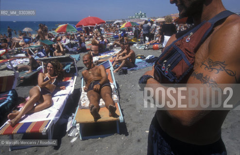 Beach bathers in Ostia Lido, 1999. Ostia is a beach town near Rome. In the summer time many people from Rome go there to the sea, particularly young suburban people said in slang coatti / Bagnanti sul Lido di Ostia, 1999. Ostia è la spiaggia dei romani. Destate è frequentata in particolare dai giovani che abitano le borgate della periferia, i cosiddetti coatti- ©Marcello Mencarini/Rosebud2