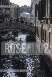 Venice, 1998. Rio di Palazzo with the Bridge of Sights in the Background. This bridge, built in 1602, passes over the Rio di Palazzo and connects the new prisons to the  old prisons in the Doges Palace. His name is because the convicts went across it before their imprisonment. A local legend says that lovers will be granted everlasting love if they kiss on a gondola at sunset under the bridge / Venezia, 1998. Il Rio di Palazzo e sullo sfondo il ponte dei Sospiri. Questo ponte è stato costruito nel 1602 e collega le vecchie prigioni che erano in Palazzo ducale con le nuove prigioni situate al di là del Rio di Palazzo. Il suo nome deriva dal fatto che di qui passavano i condannati per essere imprigionati. Secondo una leggenda, baciarsi passando sotto questo ponte in gondola al tramonto assicura agli innamorati amore eterno - ©Marcello Mencarini/Rosebud2