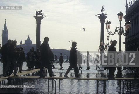 Venice, 1998. High Tide in St. Marks Square. People walking on the gangways / Venezia, 1998. Acqua alta in piazza San Marco. Passanti sulle passerelle - ©Marcello Mencarini/Rosebud2