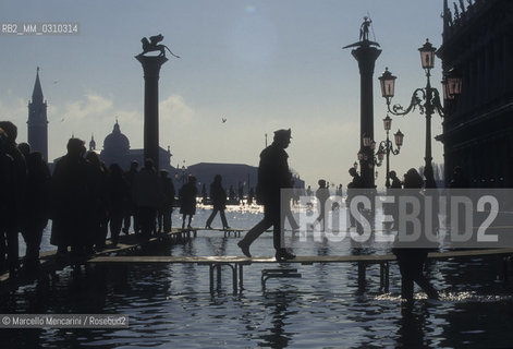 Venice, 1998. High Tide in St. Marks Square. People walking on the gangways / Venezia, 1998. Acqua alta in piazza San Marco. Passanti sulle passerelle - ©Marcello Mencarini/Rosebud2