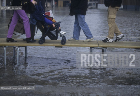 Venice, 1998. High Tide in St. Marks Square. People walking on the gangways / Venezia, 1998. Acqua alta in piazza San Marco. Passanti sulle passerelle - ©Marcello Mencarini/Rosebud2