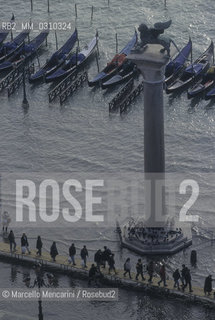 Venice, 1998. High Tide in St. Marks Square. People walking on the gangways near the St. Marks Column / Venezia, 1998. Acqua alta in piazza San Marco. Passanti sulle passerelle accanto alla Colonna di San Marco - ©Marcello Mencarini/Rosebud2