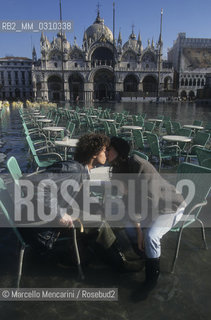 Venice, 1998. High Tide in St. Marks Square. Couple kissing at a café table / Venezia, 1998. Acqua alta in piazza San Marco. Coppia che si bacia seduta al tavolo allaperto di un bar - ©Marcello Mencarini/Rosebud2