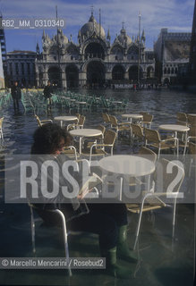 Venice, 1998. High Tide in St. Marks Square. Woman reading, sitting at the Caffè Quadri outdoors tables / Venezia, 1998. Acqua alta in Piazza San Marco. Donna che legge, seduta a un tavolo allaperto del Caffè Quadri - ©Marcello Mencarini/Rosebud2