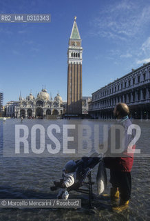 Venice, 1998. High Tide in St. Marks Square. Man with a baby buggy in the water / Venezia, 1998. Acqua alta in piazza San Marco. Uomo con passeggino in mezzo allacqua - ©Marcello Mencarini/Rosebud2