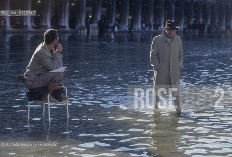 Venice, 1998. High Tide in St. Marks Square. Man walking and man sitting on a chair in the water / Venezia, 1998. Acqua alta in Piazza San Marco. Uomo che cammina e Uomo seduto su una sedia in mezzo allacqua - ©Marcello Mencarini/Rosebud2