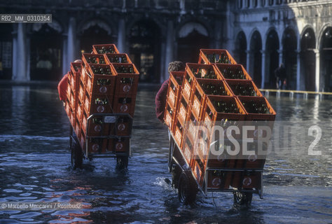 Venice, 1998. High Tide in St. Marks Square. Men carrying crates of bottles in the water / Venezia, 1998. Acqua alta in Piazza San Marco. Uomini che trasportano casse di bottiglie in mezzo allacqua - ©Marcello Mencarini/Rosebud2