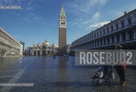 Venice, 1998. High Tide in St. Marks Square. Man pushing a baby in a stroller / Venezia, 1998. Acqua alta in Piazza San Marco. Uomo che spinge un bambino in passeggino - ©Marcello Mencarini/Rosebud2