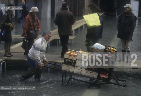 Venice, 1998. High Tide in St. Marks Square. Man carrying fruits and vegetables in the water  / Venezia, 1998. Acqua alta in Piazza San Marco. Uomo che trasporta frutta e verdura in mezzo allacqua - ©Marcello Mencarini/Rosebud2