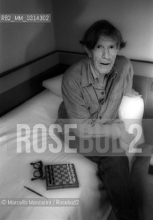 Venice, 1982. American composer John Cage sitting on the bed with a chessboard in his hotel room  / Venezia, 1982. Il compositore John Cage seduto sul letto con una scacchiera nella sua stanza dalbergo - ©Marcello Mencarini/Rosebud2