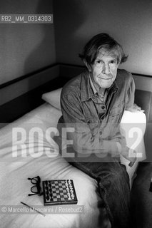 Venice, 1982. American composer John Cage sitting on the bed with a chessboard in his hotel room  / Venezia, 1982. Il compositore John Cage seduto sul letto con una scacchiera nella sua stanza dalbergo - ©Marcello Mencarini/Rosebud2