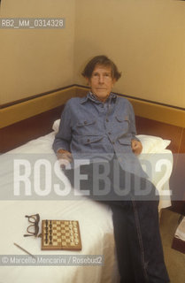 Venice, 1982. American composer John Cage sitting on the bed with a chessboard in his hotel room  / Venezia, 1982. Il compositore John Cage seduto sul letto con una scacchiera nella sua stanza dalbergo - ©Marcello Mencarini/Rosebud2