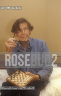 Venice, 1982. American composer John Cage sitting on the bed with a chessboard in his hotel room  / Venezia, 1982. Il compositore John Cage seduto sul letto con una scacchiera nella sua stanza dalbergo - ©Marcello Mencarini/Rosebud2