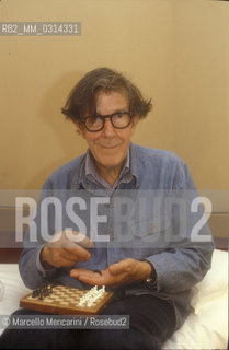 Venice, 1982. American composer John Cage sitting on the bed with a chessboard in his hotel room  / Venezia, 1982. Il compositore John Cage seduto sul letto con una scacchiera nella sua stanza dalbergo - ©Marcello Mencarini/Rosebud2