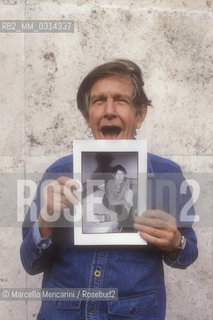 Roma, 1983. American composer John Cage holding a photo of him taken in the previous year in Venice by the same photographer / Roma, 1983. Il compositore John Cage tiene in mano una sua foto scattata lanno precedente a Venezia dallo stesso fotografo - ©Marcello Mencarini/Rosebud2