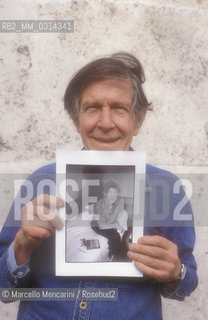 Roma, 1983. American composer John Cage holding a photo of him taken in the previous year in Venice by the same photographer / Roma, 1983. Il compositore John Cage tiene in mano una sua foto scattata lanno precedente a Venezia dallo stesso fotografo - ©Marcello Mencarini/Rosebud2
