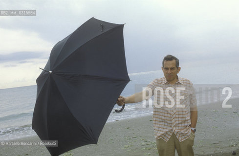 Venice, 1982. Italian composer Aldo Clementi holding an umbrella on the Lido seashore/ Venezia, 1982. Il compositore Aldo Clementi sulla spiaggia del Lido con un ombrello - ©Marcello Mencarini/Rosebud2