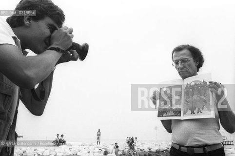 Venice Film Festival, about 1980. French cartoonist Jean Giraud (Moebius) on Venice Lido beach shot by a photographer while holding one of his drawing / Mostra del Cinema di Venezia, 1980 circa. Il disegnatore francese Jean Giraud (Moebius) sulla spiaggia del Lido mentre un fotografo lo ritrae con un suo disegno in mano- ©Marcello Mencarini/Rosebud2