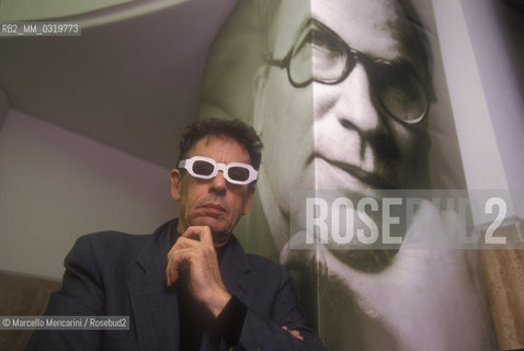 Rome, 1998. American composer Philip Glass wearing glasses to see three-dimensional images. He is in Rome at the Olympic Theater for the 3D opera Monsters of Grace, composed by him with Bob Wilson. A photo of Bob Wilson is in background / Roma, 1998. Il compositore Philip Glass con degli occhiali per immagini tridimensionali, a Roma al Teatro Olimpico con lopera Monster of Grace, scritta da lui in collaborazione con Bob Wilson. Sullo sfondo una foto di Bob Wilson - ©Marcello Mencarini/Rosebud2