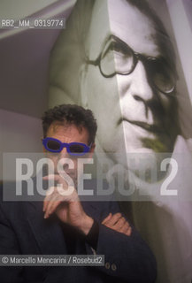 Rome, 1998. American composer Philip Glass wearing glasses to see three-dimensional images. He is in Rome at the Olympic Theater for the 3D opera Monsters of Grace, composed by him with Bob Wilson. A photo of Bob Wilson is in background / Roma, 1998. Il compositore Philip Glass con degli occhiali per immagini tridimensionali, a Roma al Teatro Olimpico con lopera Monster of Grace, scritta da lui in collaborazione con Bob Wilson. Sullo sfondo una foto di Bob Wilson - ©Marcello Mencarini/Rosebud2