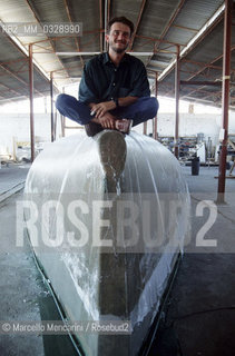 July 1993. Italian sailor Giovanni Soldini in the Toxic Boat shipyards, sitting on the hull of his boat to sail solo around the world, built by former drug addicts of the Saman Community / Luglio 1993. Il velista Giovanni Soldini nei cantieri Toxic Boat di Latina, seduto sullo scafo della sua barca per il giro del mondo in solitaria realizzato dagli ex tossicodipendenti della Comunità Saman - ©Marcello Mencarini/Rosebud2