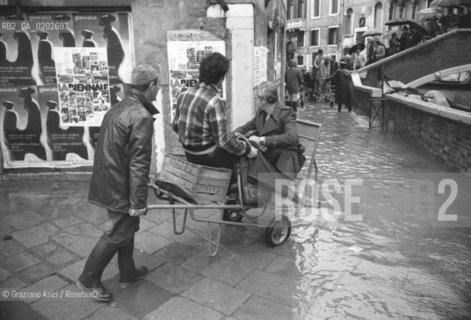 VENEZIA 1975 ACQUA ALTA © ARCHIVIO Graziano Arici/Rosebud2  VENEZIA ACQUA ALTA PERSONE PONTE CARRETTO PORTAPERSONE MANIFESTI BIENNALE