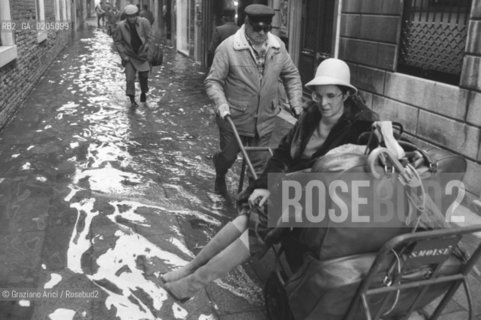 VENEZIA 1981 ACQUA ALTA IN CALLE © ARCHIVIO Graziano Arici/Rosebud2  ALTA MAREA PROBLEMI DISAGI VENEZIA UOMO CON CARRETTO PORTAPERSONE FACCHINO