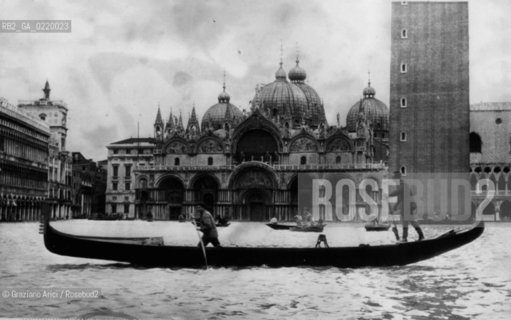 Venice,1951. Piazza San Marco. Due uomini conducono una gondola durante lalta marea. Sullo sfondo la Basilica. Two men guide a gondola through flooded St. Marks Square. In background are St. Marks Cathedral. Acqua alta; alta marea La cessione dei diritti si intende per quanto di nostra competenza; non comprende invece le eventuali spese relative a diritti che potranno essere richiesti dagli Enti cui appartengono le opere riprese. Tali costi, ove neccessari, e l’espletamento di qualsivoglia pratica di richiesta permessi sono esclusivamente  a  carico del committente. © ARCHIVIO Graziano Arici/Rosebud2 