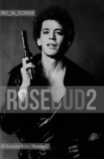 -Fine anni 70. Ritratto del cantautore e chitarrista rock Lou Reed, con una pistola. Musica cantante cantautore chitarrista rock ritratto pistola.-Late 70. Portrait of the singer and guitarist Lou Reed with a pistol - Archivio Graziano Arici..Avvertenze relative al copyright delle immagini.Le immagini riprodotte sono state eseguite per promuovere il prodotto culturale di cui in didascalia..La possibilità di utilizzare queste immagini è riservata unicamente al fine di corredare con le stesse, servizi, articoli, segnalazioni inerenti liniziativa cui si riferiscono. .La cessione dei diritti di questa immagine si intende per quanto di nostra competenza. Non comprende invece le eventuali spese  relative a diritti che potranno essere richiesti dagli Enti o persone fisiche cui appartengono eventualmente i soggetti  ripresi. Tali costi, ove necessari, e l’espletamento di qualsivoglia pratica di richiesta di concessione del permesso di pubblicazione sono esclusivamente a carico e a cura del soggetto acquirente di questa immagine..