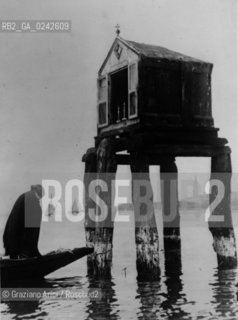 -Venezia,anni 30. Laguna di Venezia.Un capitello costruito su delle bricole in acqua e un fedele in preghiera da una barca. Capitello Laguna acqua preghiera.-Venice, 30 Years. Simple shrine set on spiles in the Grand Canal of Venice - Archivio Graziano Arici.LArchivio Arici non è riuscito ad avere informazioni sullautore di questa foto. Siamo comunque a disposizione di qualunque avente diritto per riconoscere eventuali proprietà intellettuali che non sia stato possibile fin qui attribuire. .Qualora si fosse inavvertitamente leso qualsiasi diritto di riproduzione, si prega di contattare lArchivio che provvederà a rimuovere le immagini in questione..La cessione dei diritti di questa immagine si intende per quanto di nostra competenza. Non comprende invece le eventuali spese  relative a diritti che potranno essere richiesti dagli Enti o persone fisiche cui appartengono eventualmente i soggetti  ripresi. Tali costi, ove necessari, e l’espletamento di qualsivoglia pratica di richiesta di concessione del permesso di pubblicazione sono esclusivamente a carico e a cura del soggetto acquirente di questa immagine..