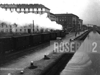 Milan, about 1930. El Gamba de legn (the Wooden Leg) along the Naviglio Pavese canal. It was a suburban train hauled by a German steam locomotive, manufactured by Krauss Lokomotivenfabrik / Milano, 1930 circa. El Gamba del legn lungo il Naviglio pavese. Si chiamavano Gamba de legni convogli extraurbani trainati da una locomotiva a vapore tedesca, fabbricata dalla Lokomotivenfabrik Krauss - Reproduced by MaMoArchives/Rosebud2