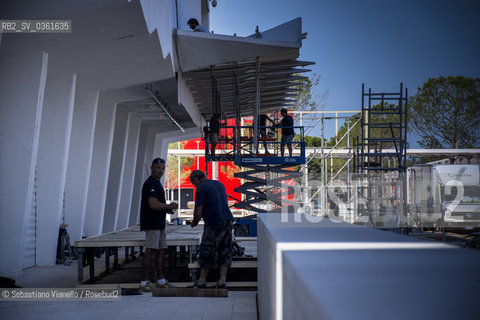 Lido di Venezia, 21 Agosto 2017. Lavori di allestimento del Palazzo del Cinema per la 74a edizione della Mostra Internazionale del Cinema di Venezia. Due operai in pausa bevono un caffè appogiati ad un praticabile mentre altri operai sullo sfondo proseguono il loro lavoro su una impalcatura mobile. ©Sebastiano Vianello/Rosebud2