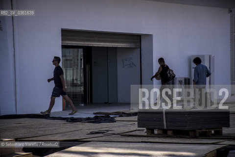 Lido di Venezia, 21 Agosto 2017. Lavori di allestimento del Palazzo del Cinema per la 74a edizione della Mostra Internazionale del Cinema di Venezia.Tre addetti ai lavori camminano nei pressi di una delle entrate del Palazzo del Cinema. ©Sebastiano Vianello/Rosebud2