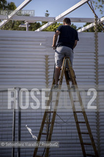 Lido di Venezia, 21 Agosto 2017. Lavori di allestimento del Palazzo del Cinema per la 74a edizione della Mostra Internazionale del Cinema di Venezia. Un operaio in piedi su una scala lavora alla costruzione di una della strutture prefabbricate nel piazzale del Palazzo del Casinò. ©Sebastiano Vianello/Rosebud2