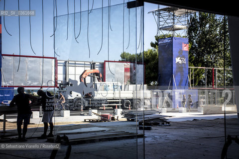 Lido di Venezia, 21 Agosto 2017. Lavori di allestimento del Palazzo del Cinema per la 74a edizione della Mostra Internazionale del Cinema di Venezia. Lingresso del Palazzo del Cinema visto dallinterno dellentrata principale. Due operai in controlucelavorano ad alcuni cavi elettrici pendenti dalla pensilina esterna del palazzo. ©Sebastiano Vianello/Rosebud2